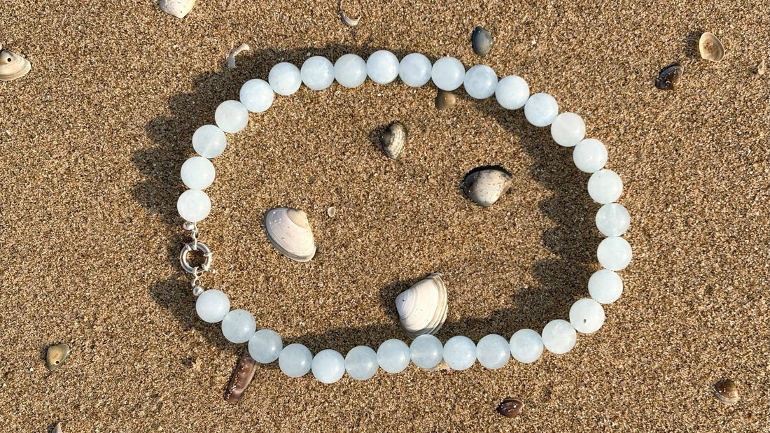 Pale blue aquamarine bead necklace with 925 sterling silver clasp on beach sand with seashells